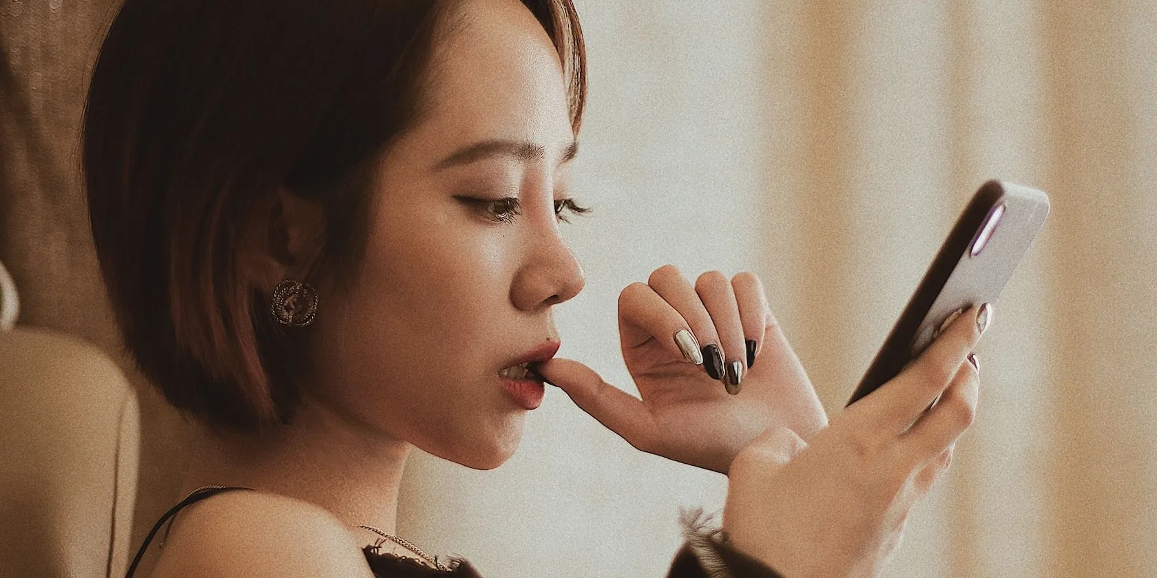 امرأة تحدق في هاتف ذكي مع إصبع في فمها