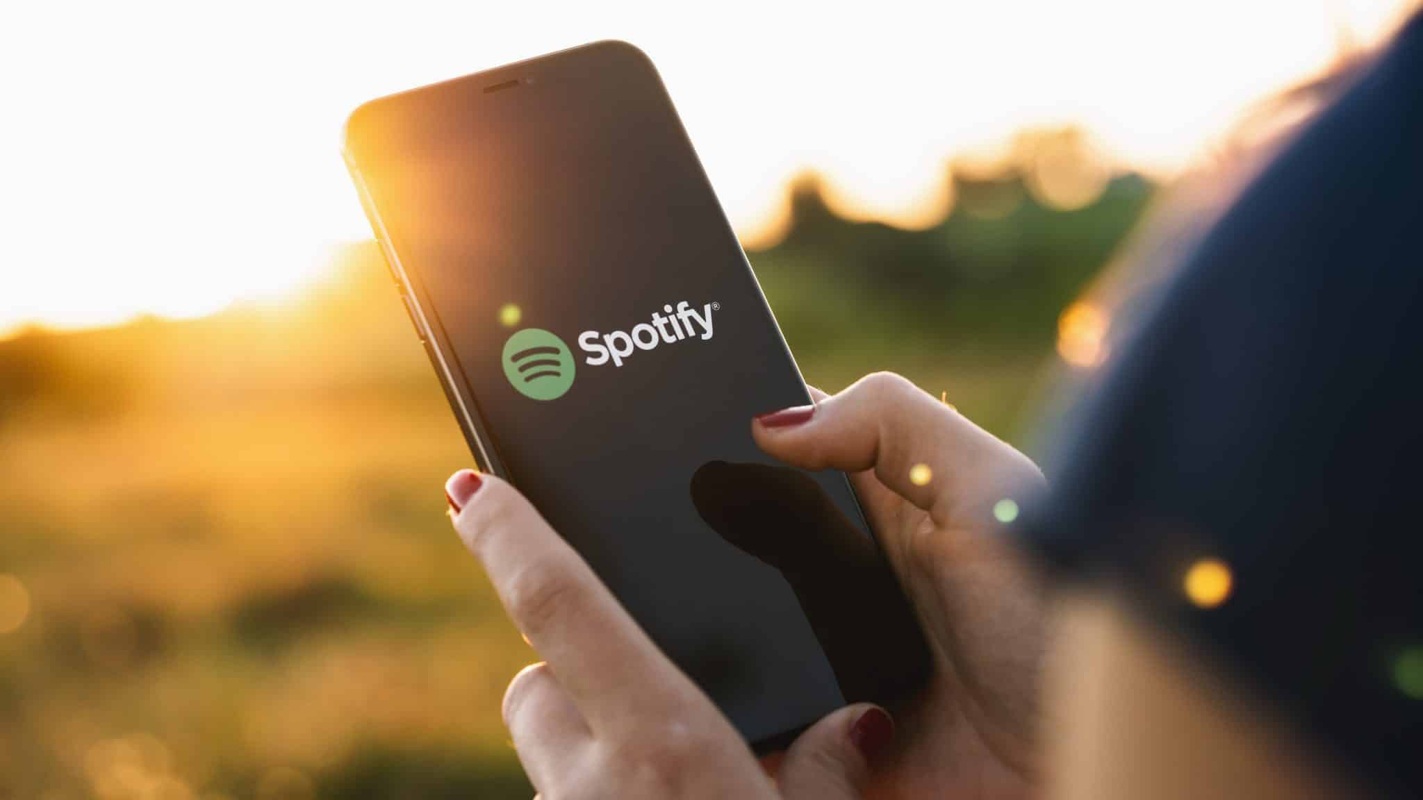 امرأة تحمل هاتفًا في حقل مع ظهور تطبيق Spotify على الشاشة