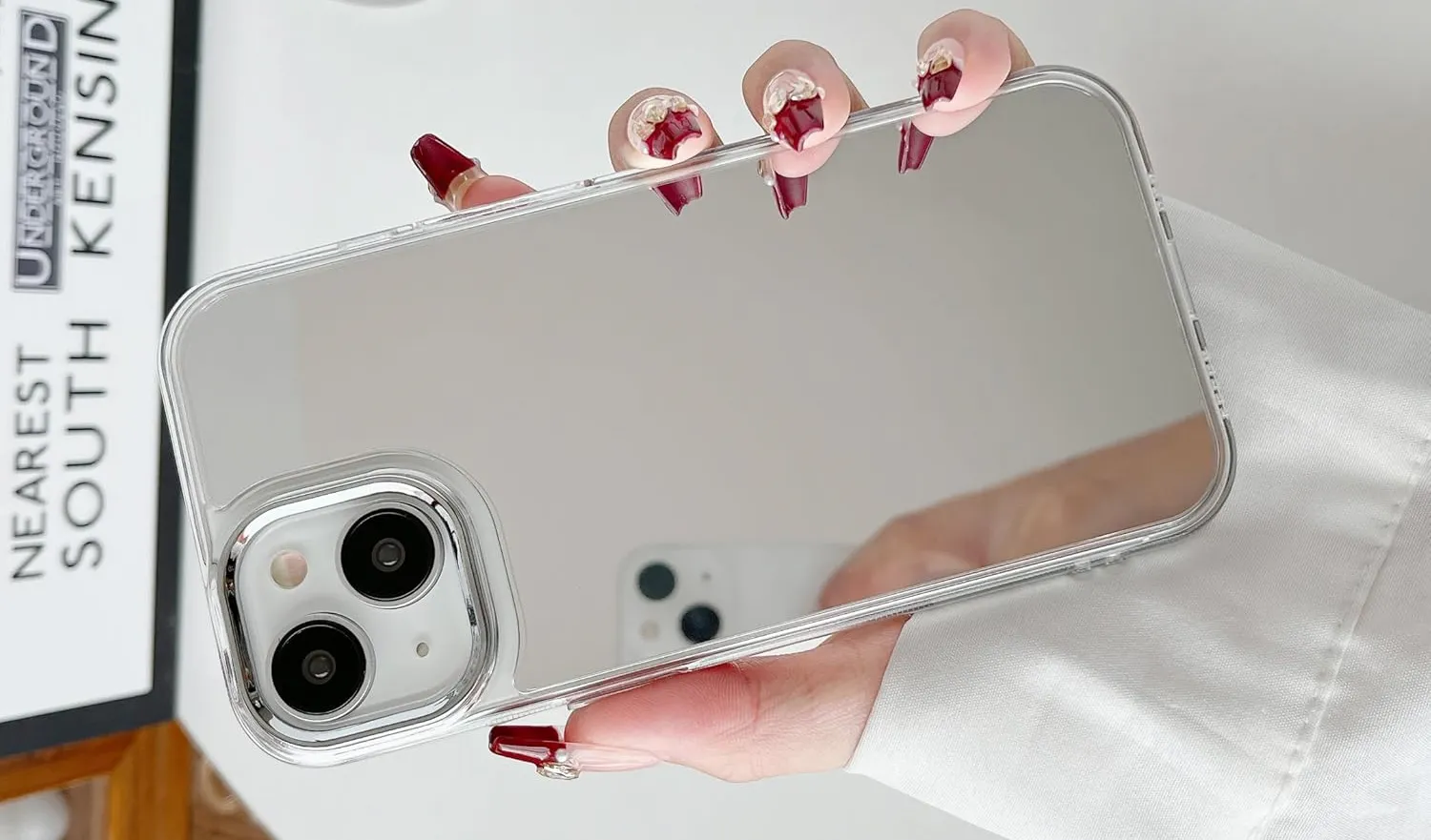 A hand holding an iPhone with a reflective mirror case.