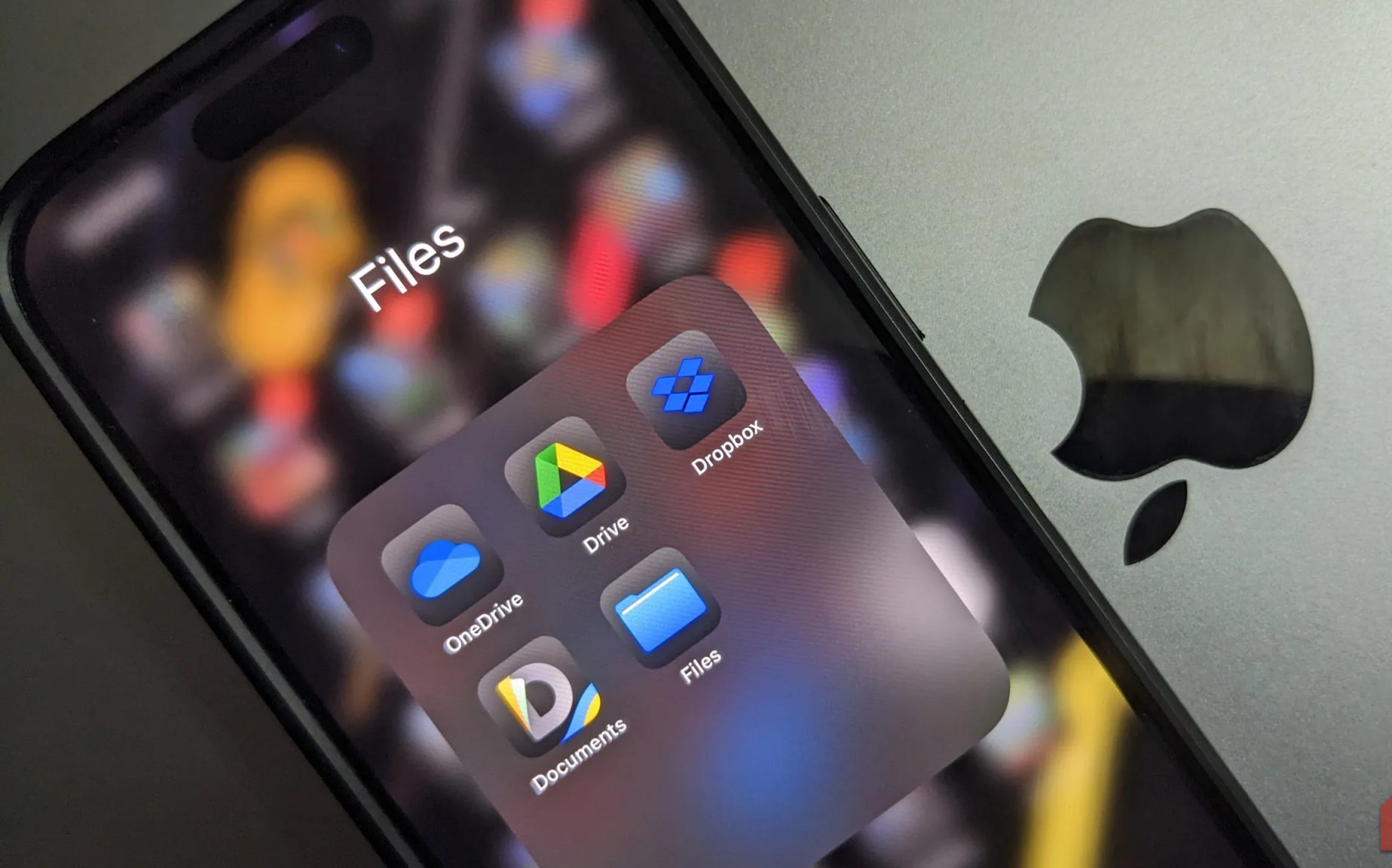 مجلد تطبيقات التخزين السحابي على جهاز iPhone موضوع فوق جهاز MacBook بشعار Apple