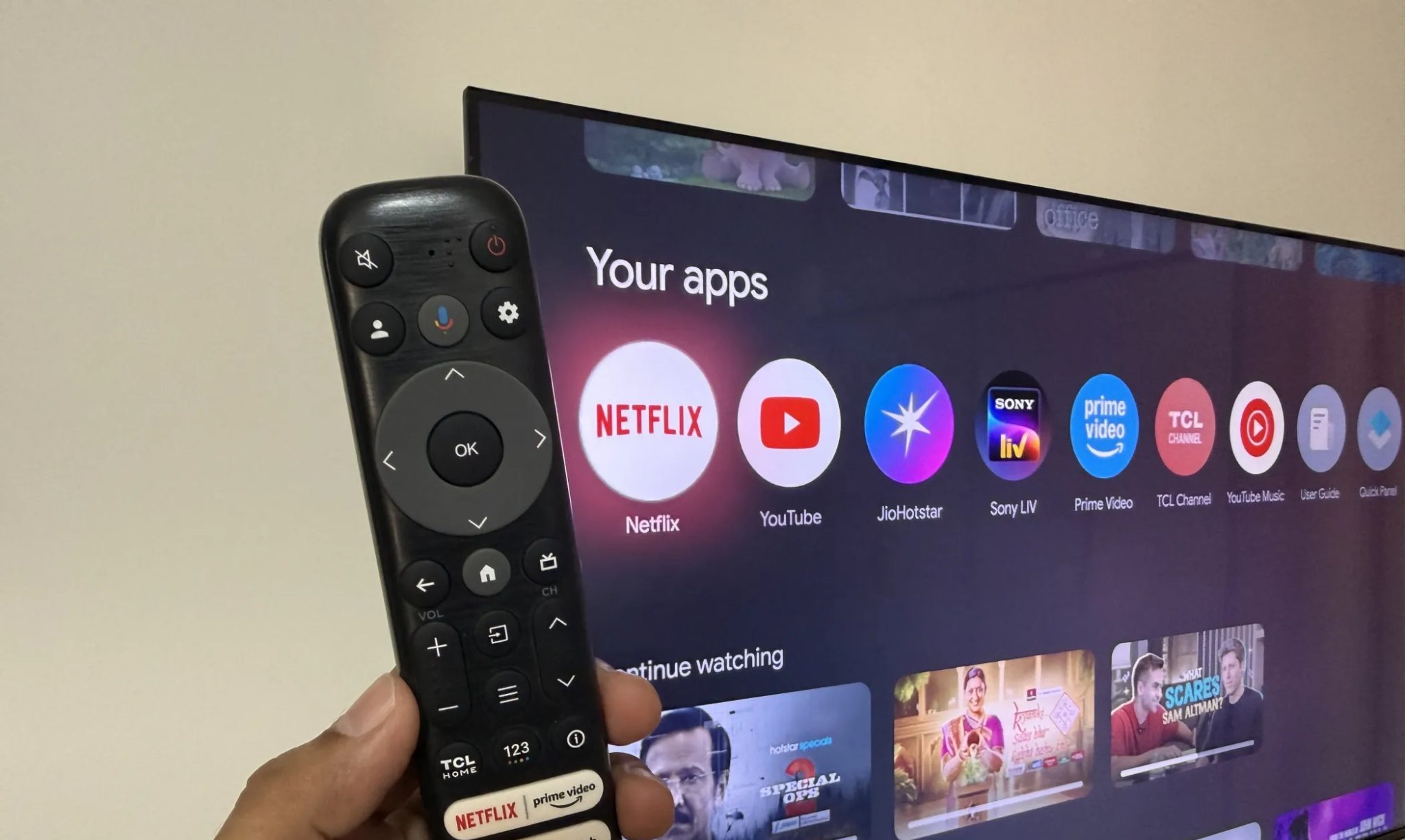 يد تحمل جهاز تحكم عن بعد مع Google TV في الخلفية