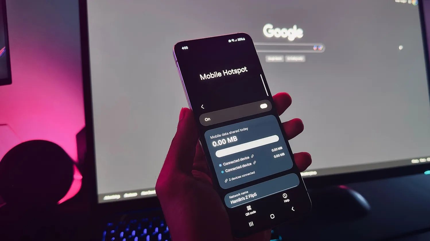 يد تحمل هاتف Android يعرض ميزة نقطة الاتصال المحمولة أمام شاشة الكمبيوتر
