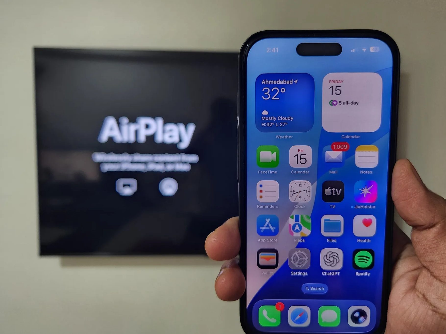 هاتف iPhone في اليد مع تلفزيون يعرض AirPlay في الخلفية
