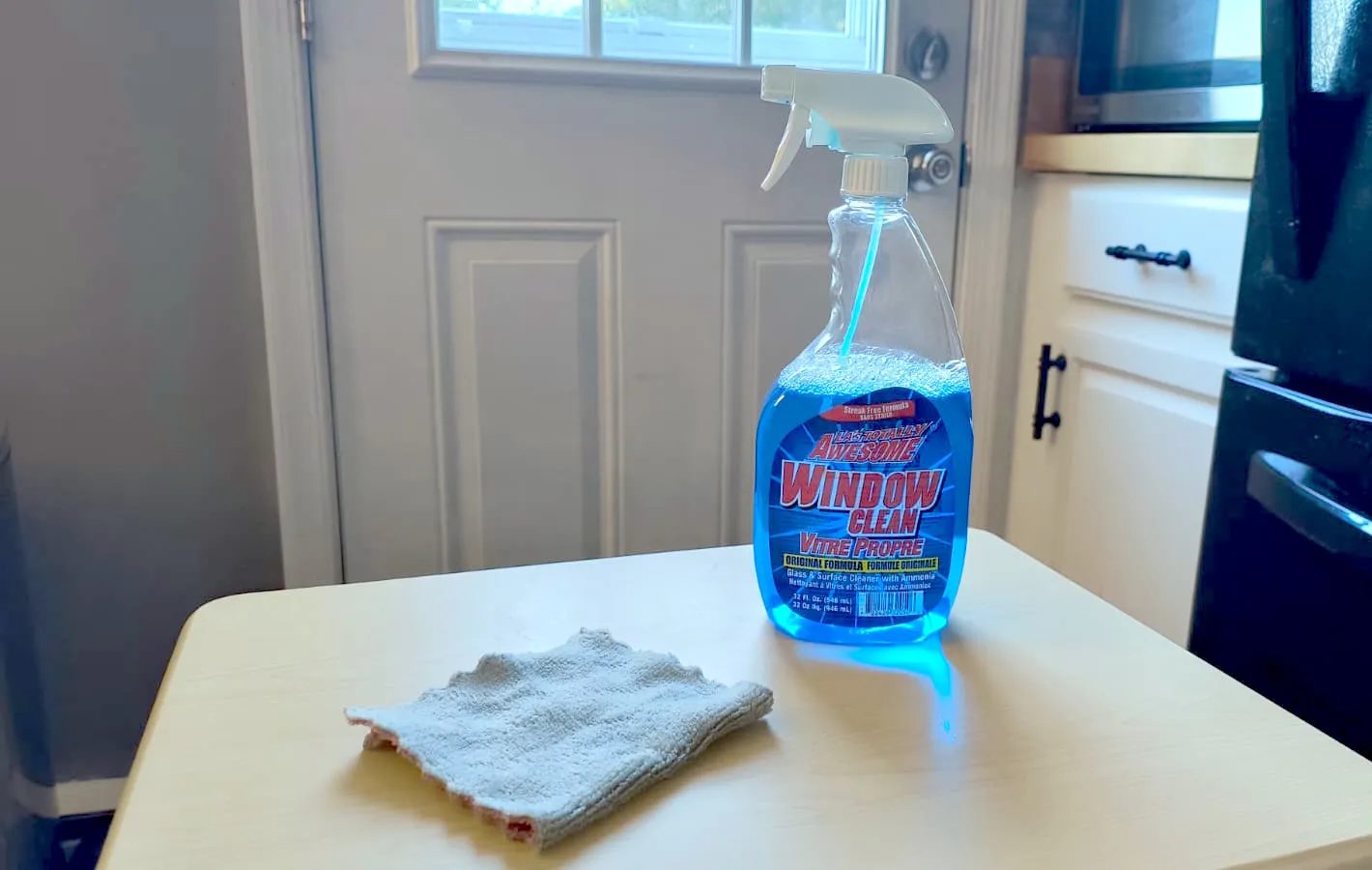 A bottle of window washing solution next to a microfiber cloth on a small table