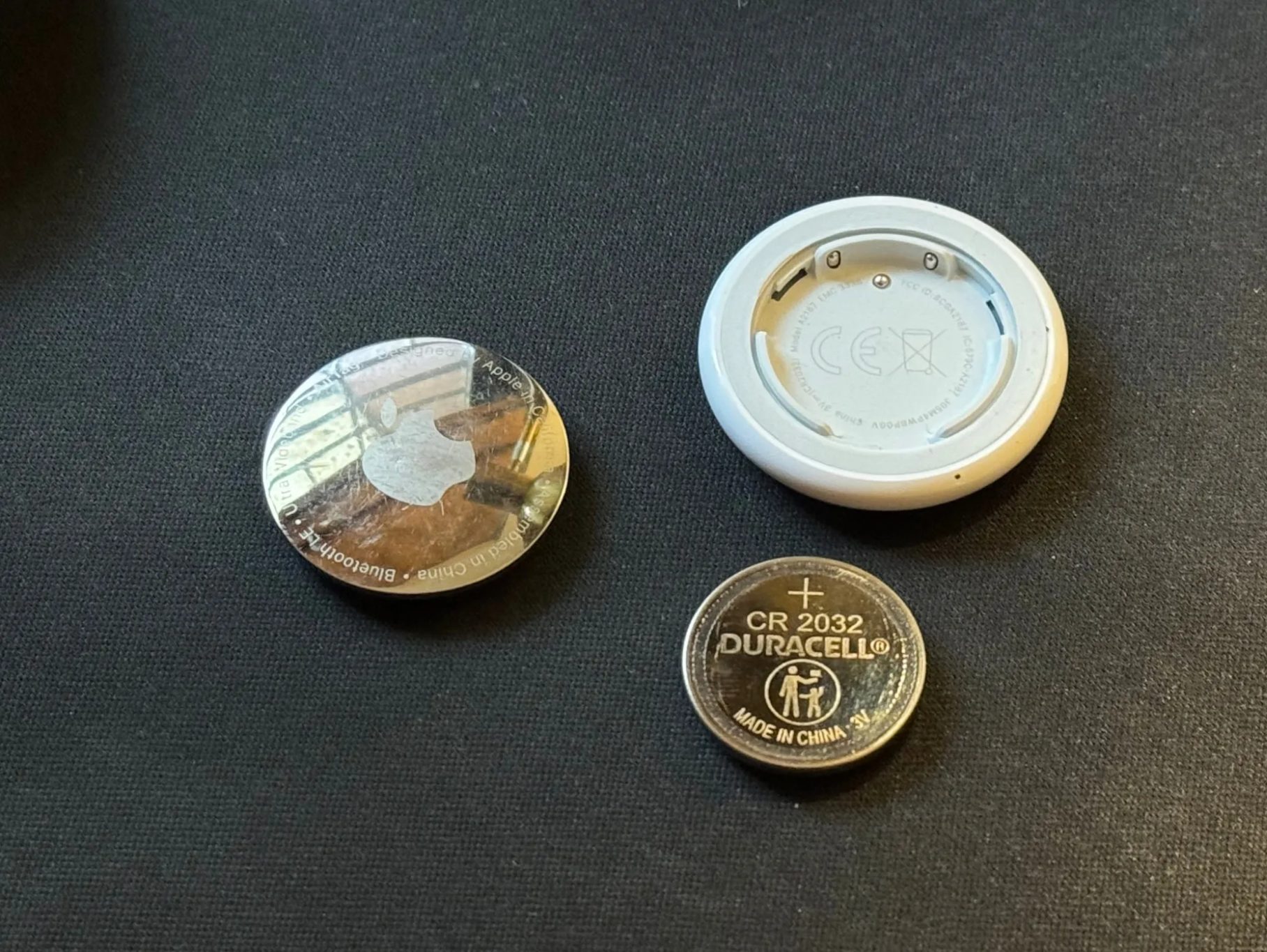 A disassembled AirTag placed on a black mat along with its CR 2032 cell