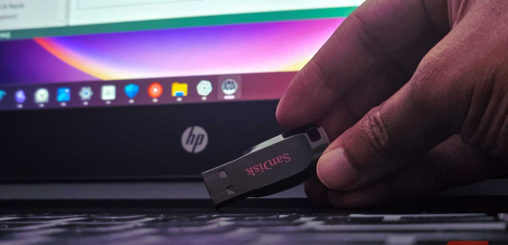 Human hand holding a sandisk USB drive on a laptop keyboard