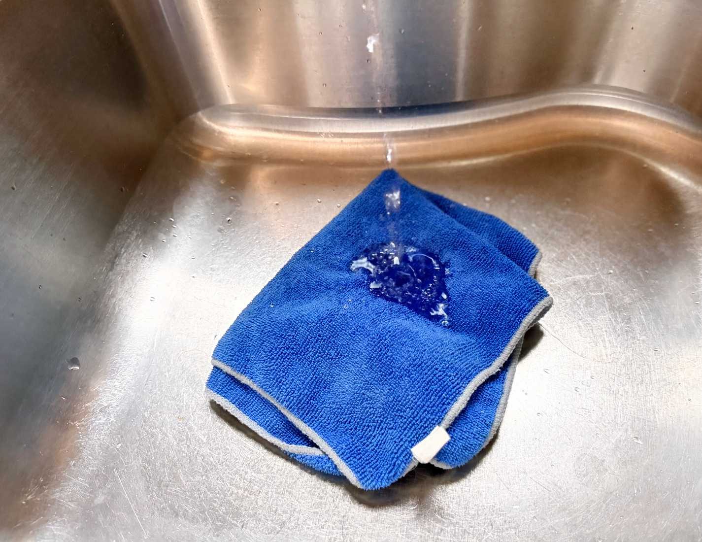 قطعة قماش زرقاء من الألياف الدقيقة في حوض يتم رشها بالماء.